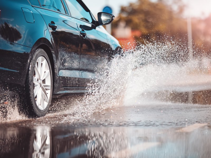 Schwarzes Auto fährt durch eine nasse Senke und erzeugt eine große Wasserwelle.